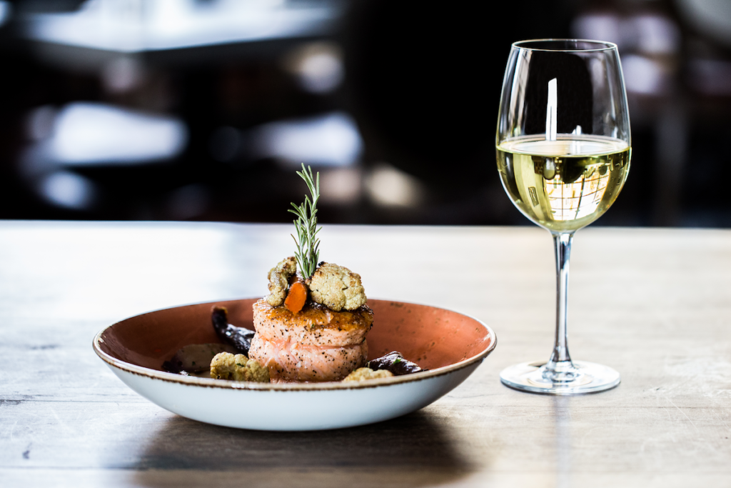 Image of Salmon dish next to glass of white wine on wooden table